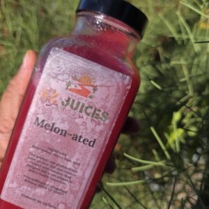 Hand holding red Melon-ated juice bottle outdoors