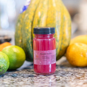Small pink juice bottle among assorted fruits